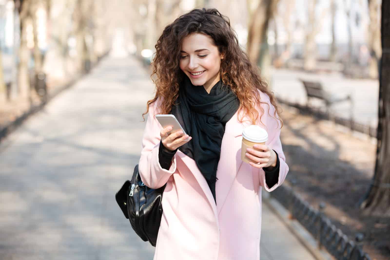 una donna sorridente con i capelli crespi è in piedi sulla strada e telefona al telefono