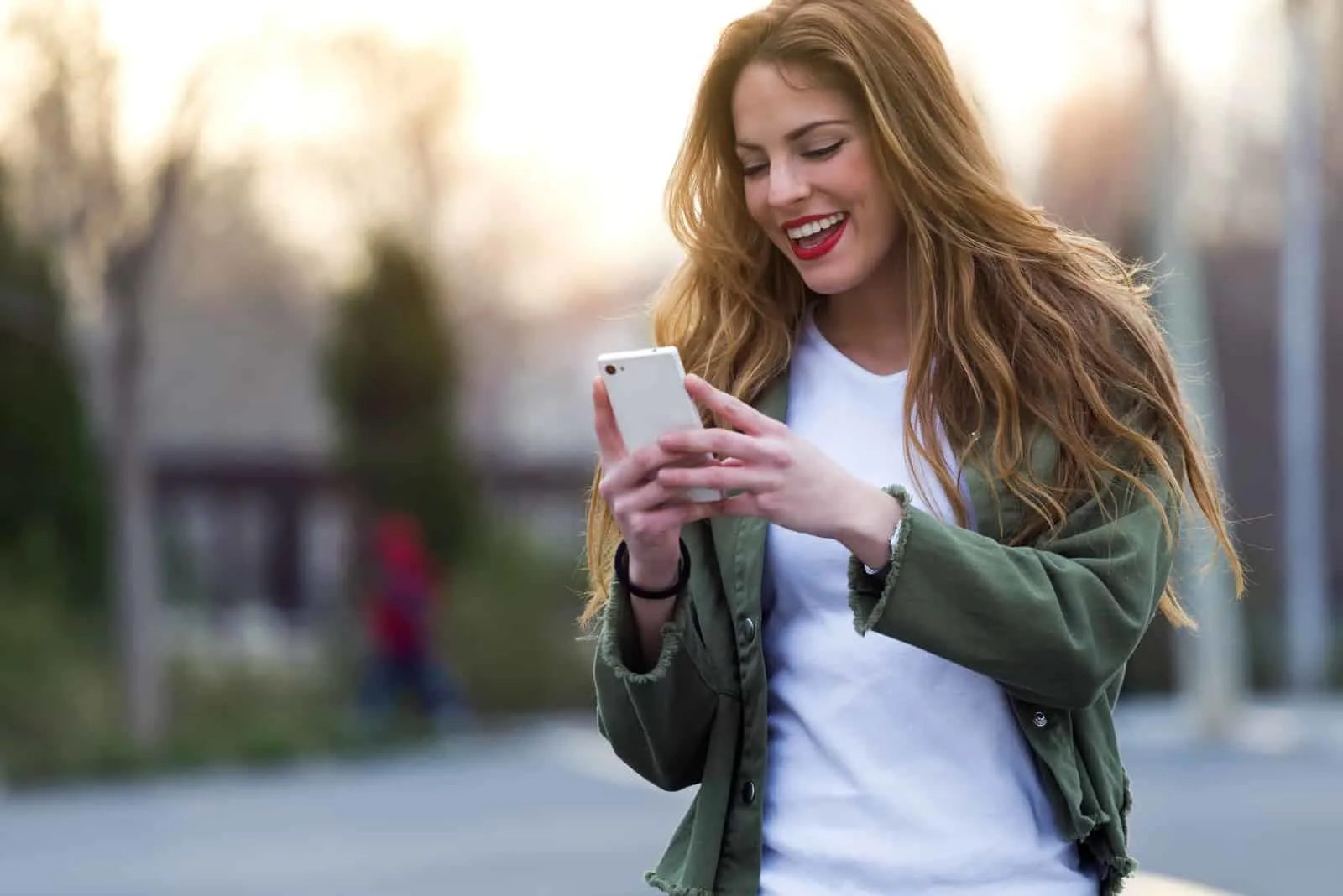 a smiling woman with long brown hair walks down the street and buttons on the phone