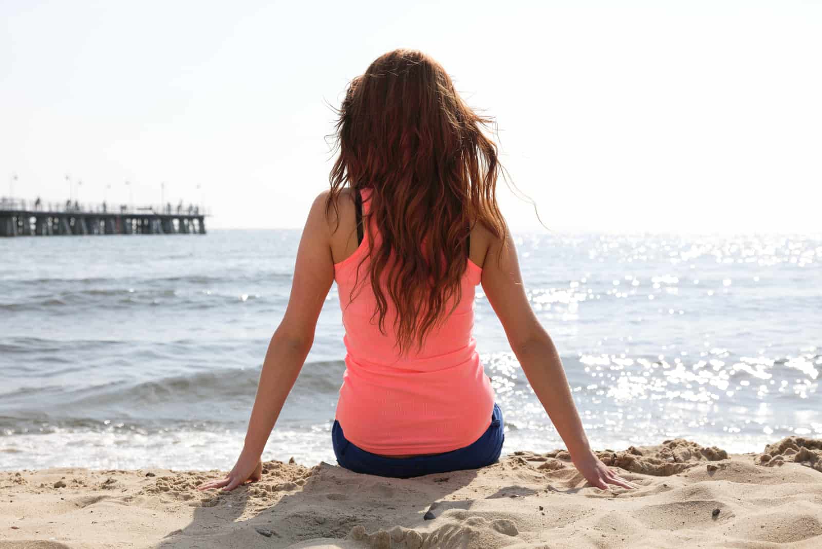 a woman with long brown hair sitting on the beach