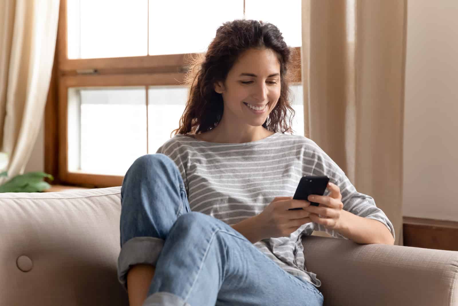 cute happy girl sitting on sofa on her phone