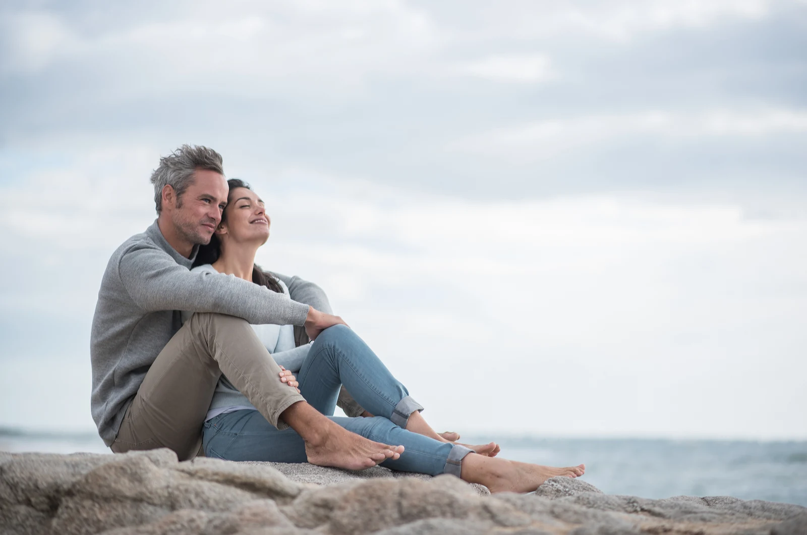 happy couple sitting on rock by sea