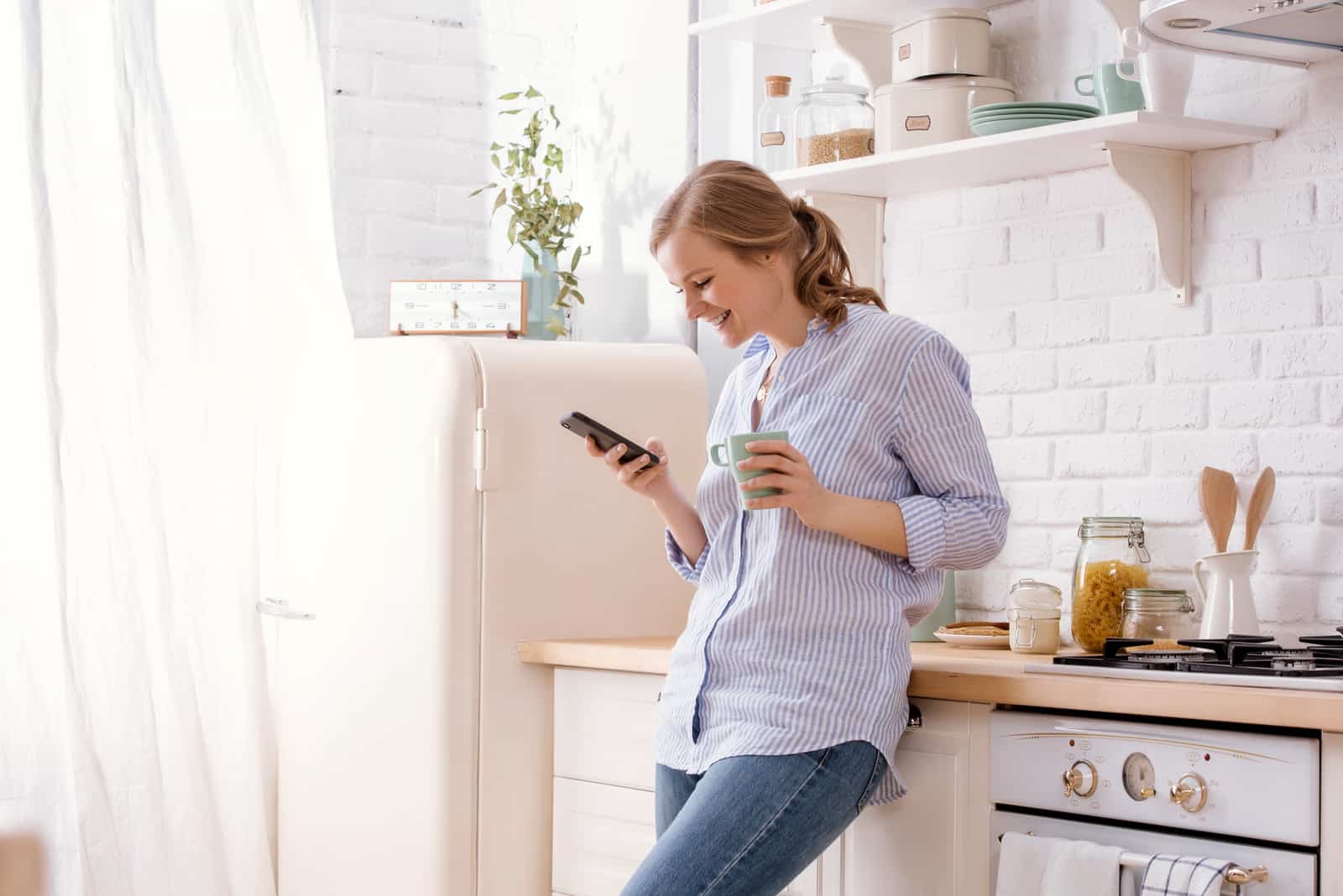 donna felice che legge i messaggi in piedi in cucina