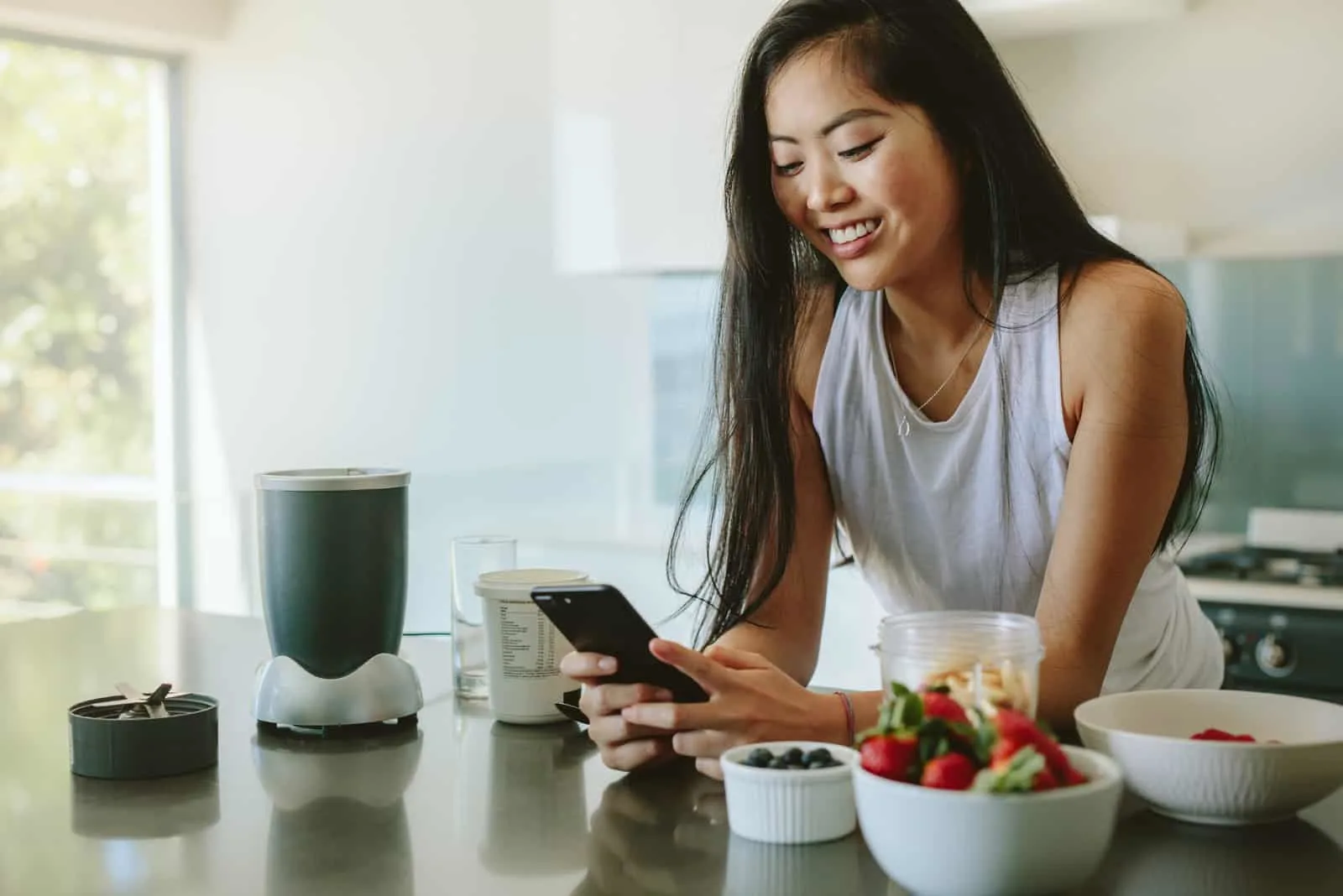 happy woman standing in kitchen texting her friends