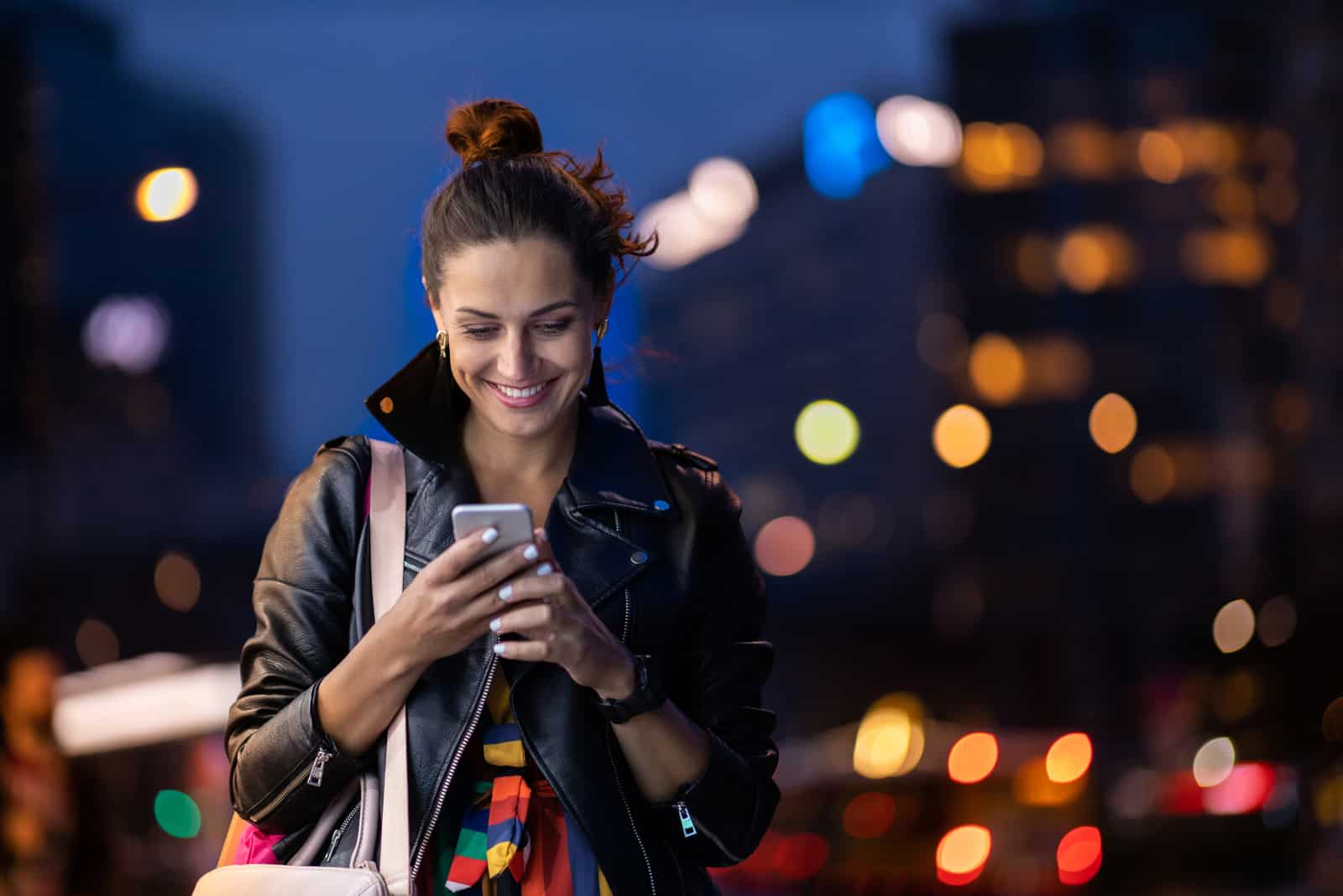 mujer feliz enviando mensajes de texto mientras camina a casa por la noche