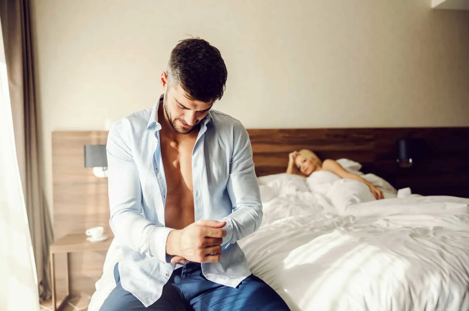 man getting ready with woman in bed in background