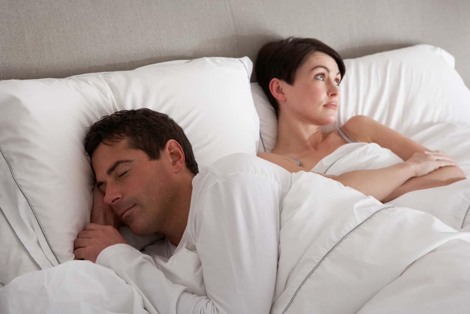 man sleeping in bed while woman in mad