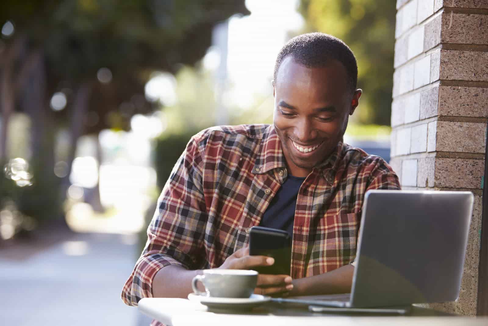 uomo sorridente seduto all'aperto e che preme al telefono