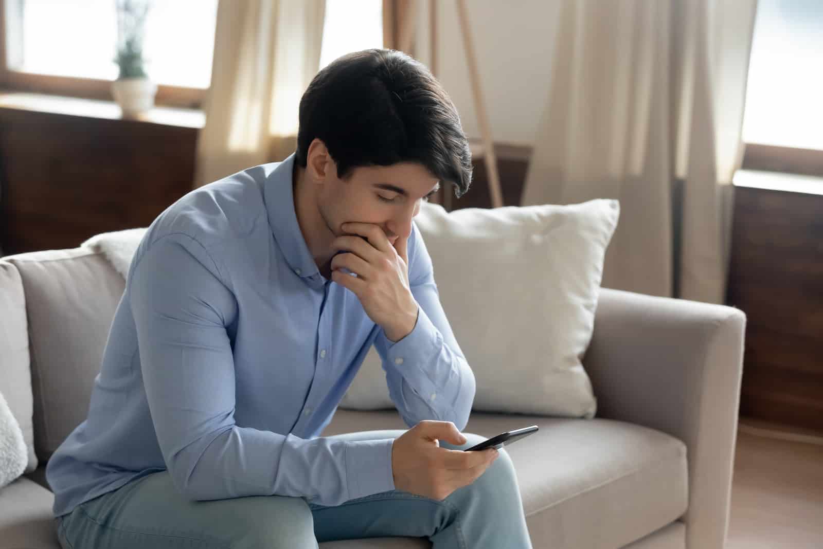 homem cansado sentado no sofá com o telemóvel na mão