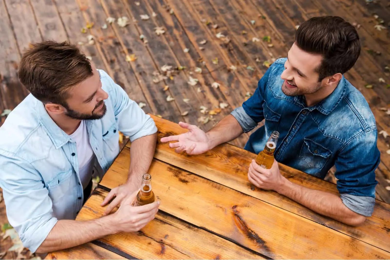 two men sit at a table outdoors and talk