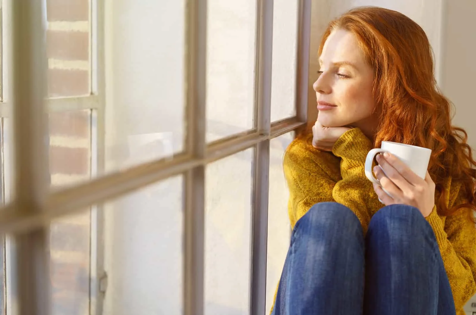 woman looking through window with cup of tea in hand