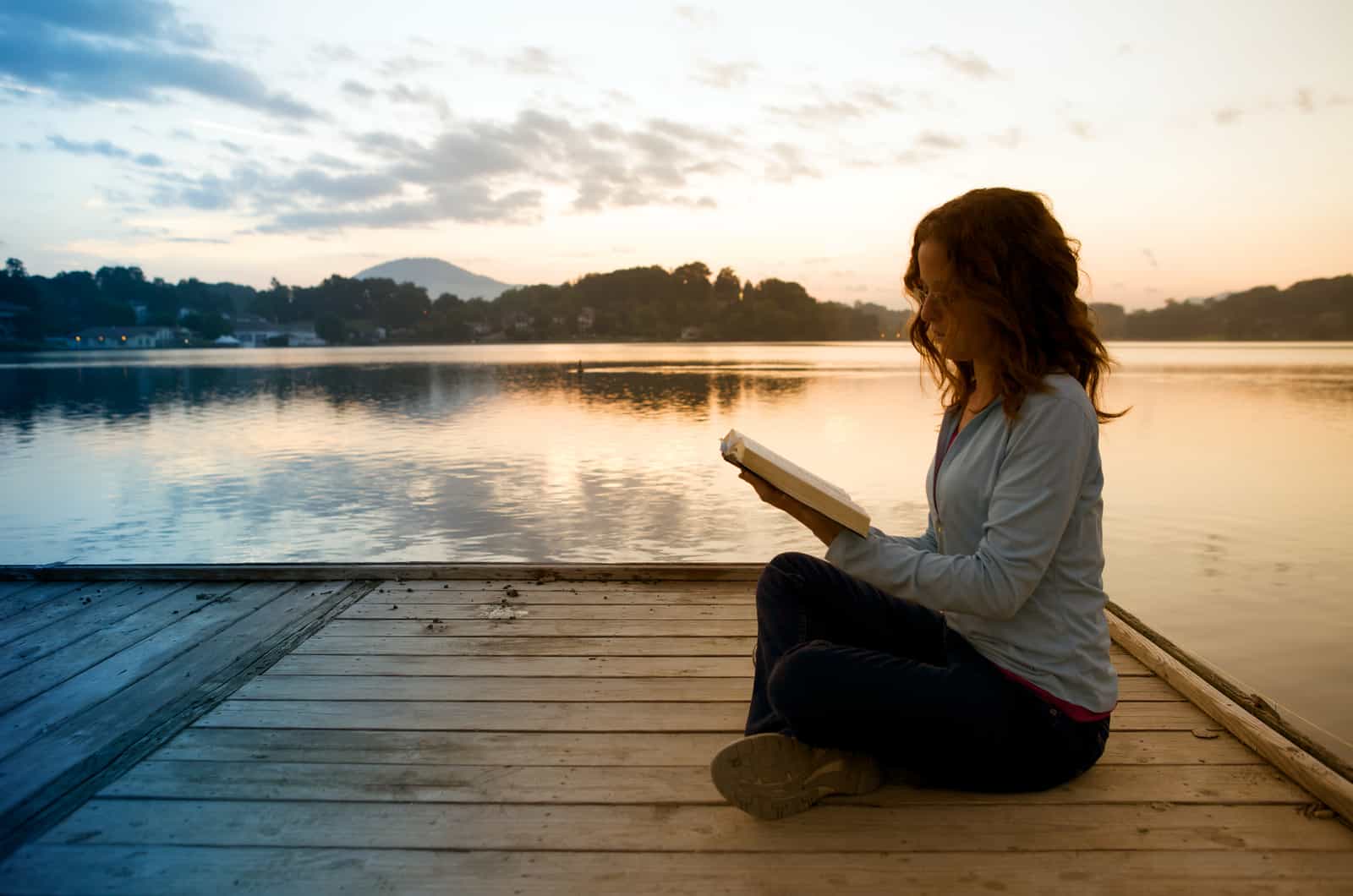 woman reading bible on dock by lake