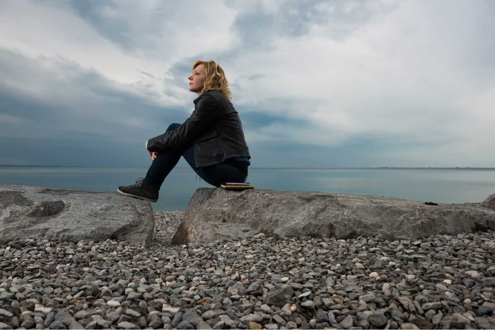 mulher sentada numa rocha a olhar para o mar