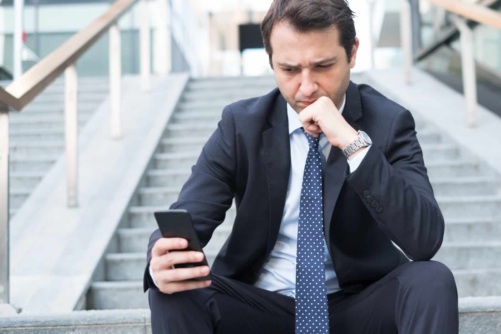 uomo preoccupato seduto sulle scale che legge i suoi messaggi