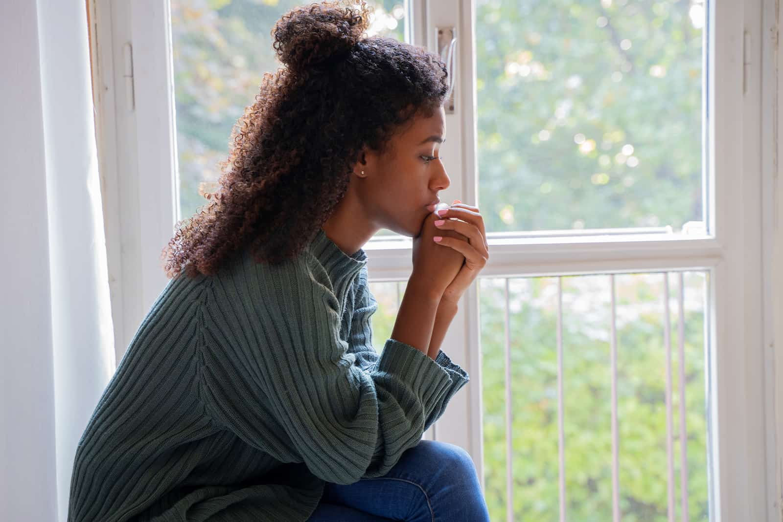 giovane ragazza seduta alla finestra che prega