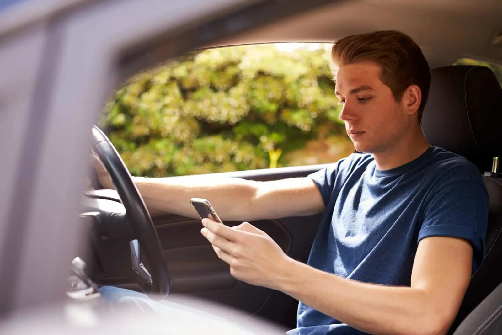 young man texting while sitting in his car
