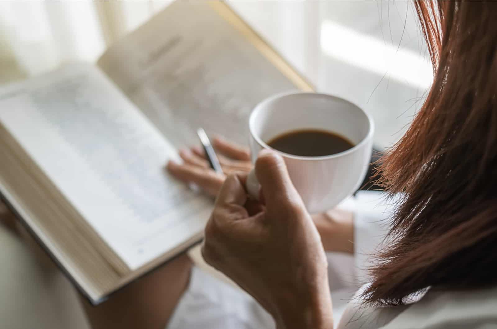 mujer joven con una taza de café en la mano leyendo