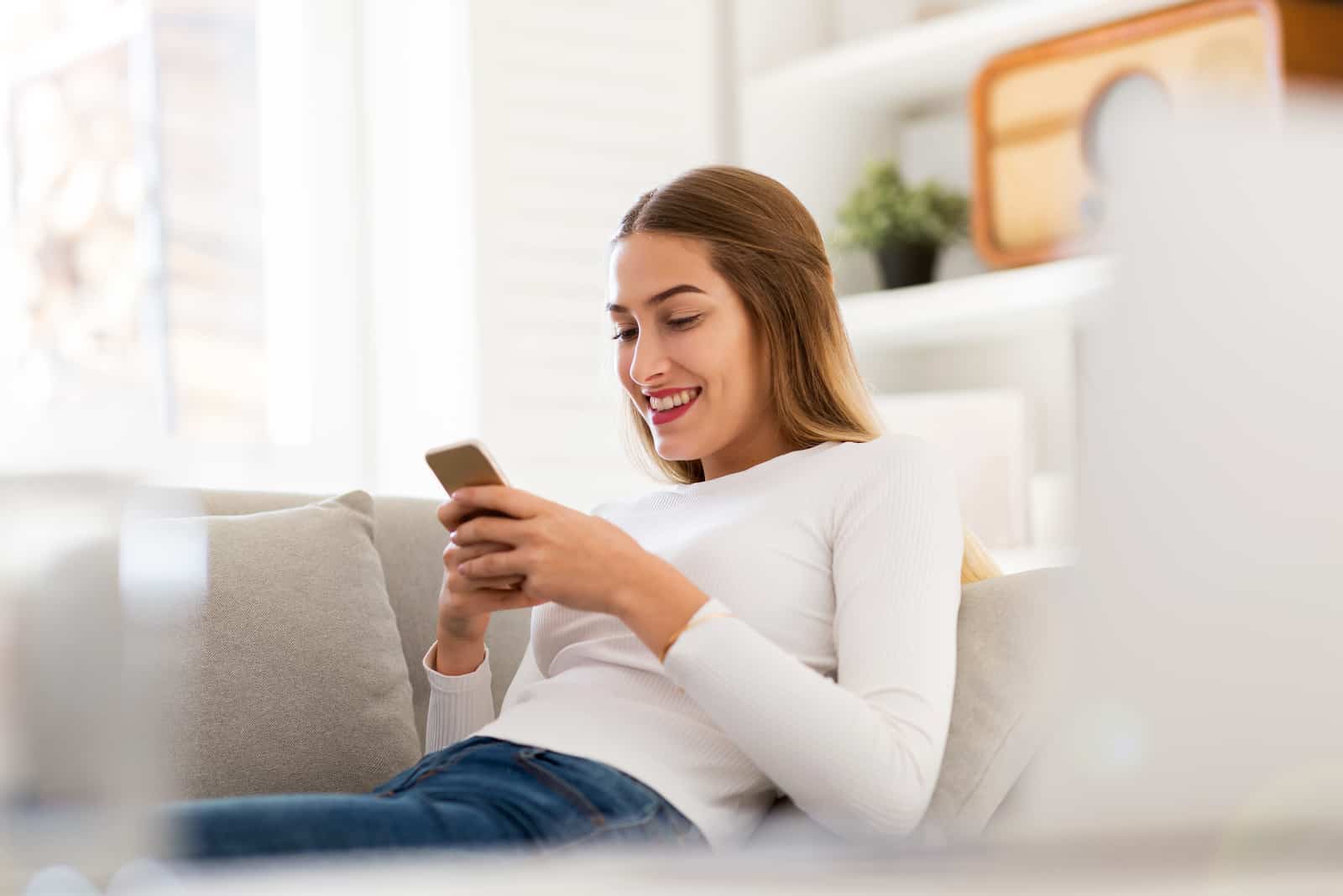 giovane donna in camicia bianca seduta sul divano che guarda il suo telefono