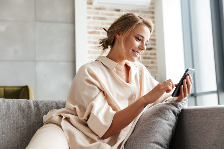 una mujer sonriente sentada en el sofá y pulsando el teléfono