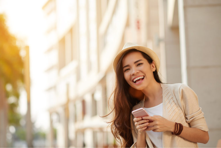 a smiling woman with a hat on her head stands and a button on the phone