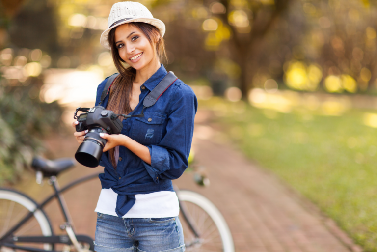 a smiling woman with a tuft on her head stands with a camera in her hand