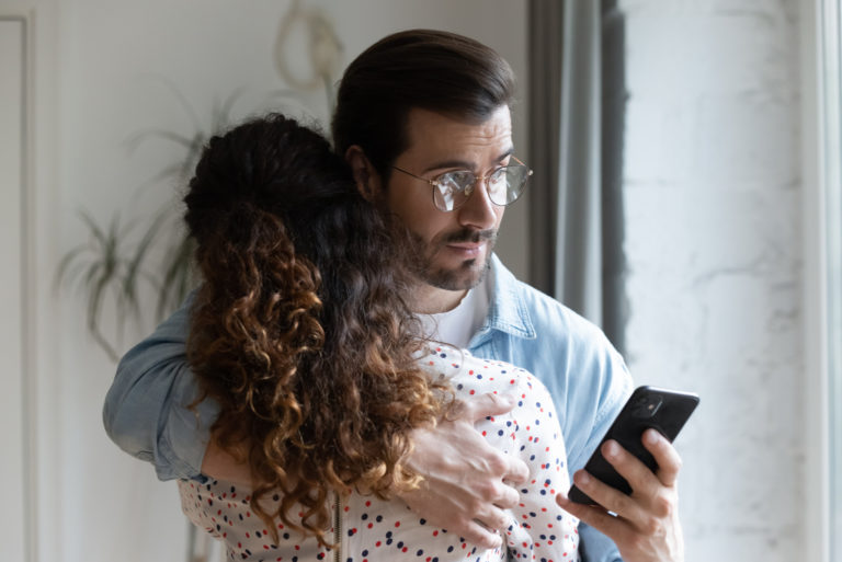 Young husband hugs wife and holds cellphone
