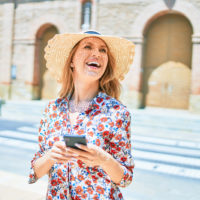 a smiling woman with a hat on her head stands in the street and buttons on the phone