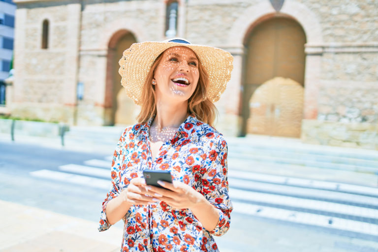 una mujer sonriente con un sombrero en la cabeza se para en la calle y llama por teléfono
