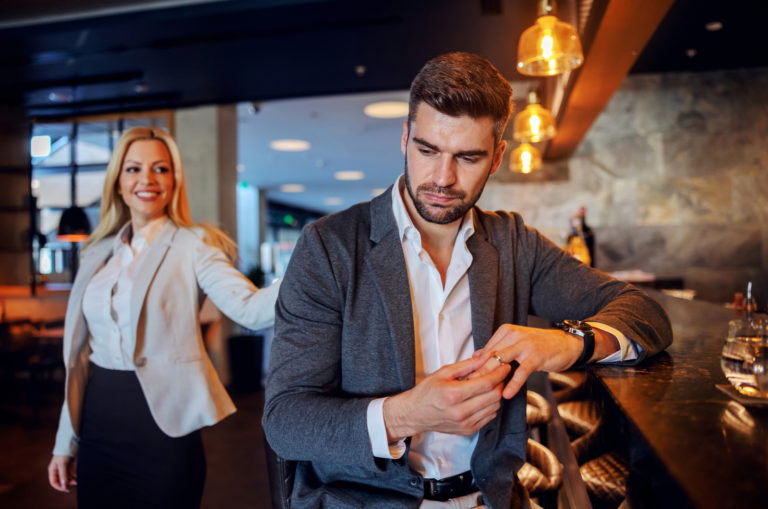 hombre sentado en un bar quitandose el anillo de boda