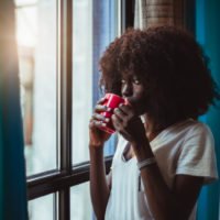 girl drinking coffe and standing by window