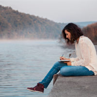 woman writing in her notebook while sitting on dock