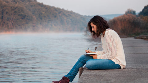 woman writing in her notebook while sitting on dock