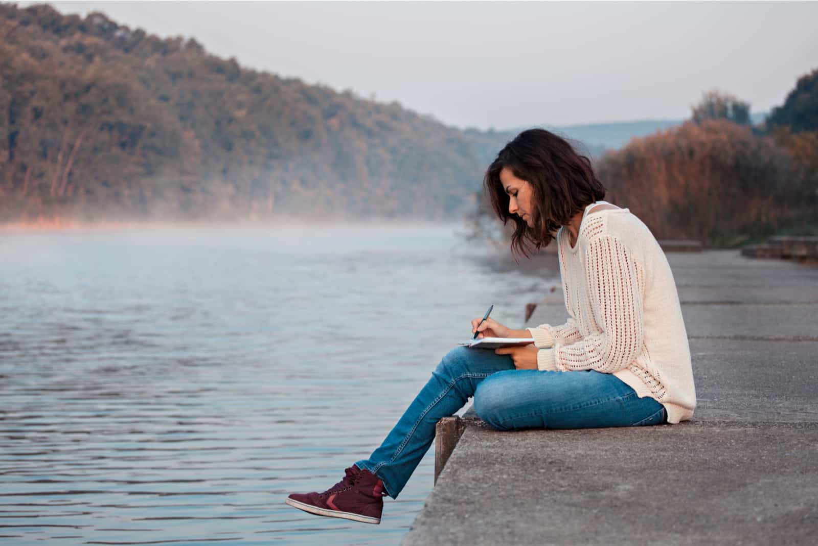 woman writing in her notebook while sitting on dock