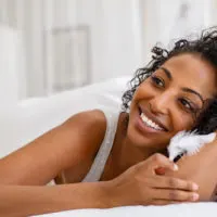 a smiling woman lies in bed and holds a white feather in her hand