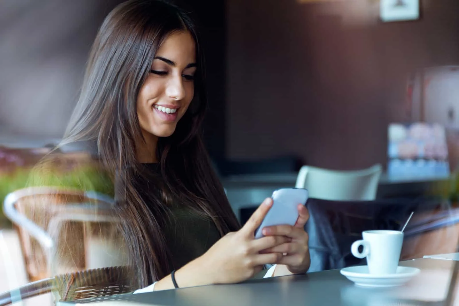 a beautiful woman with long black hair sits at a table and keys on the phone
