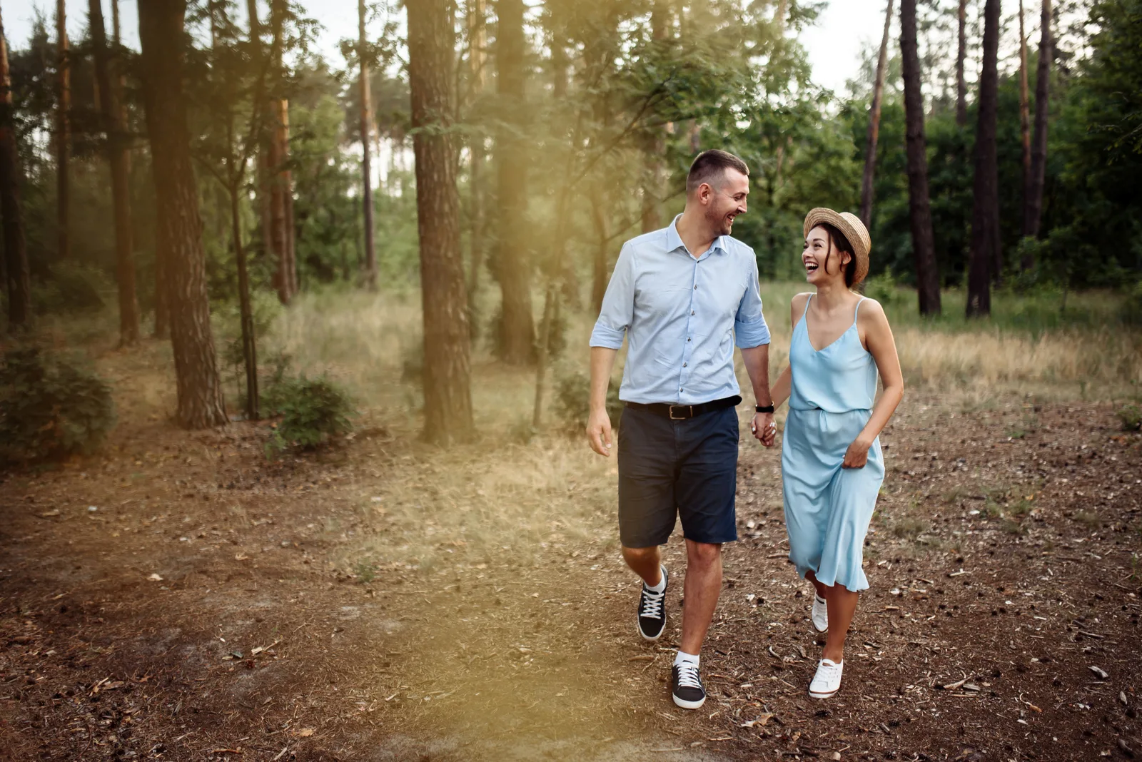 a smiling man and woman holding hands and walking through the park