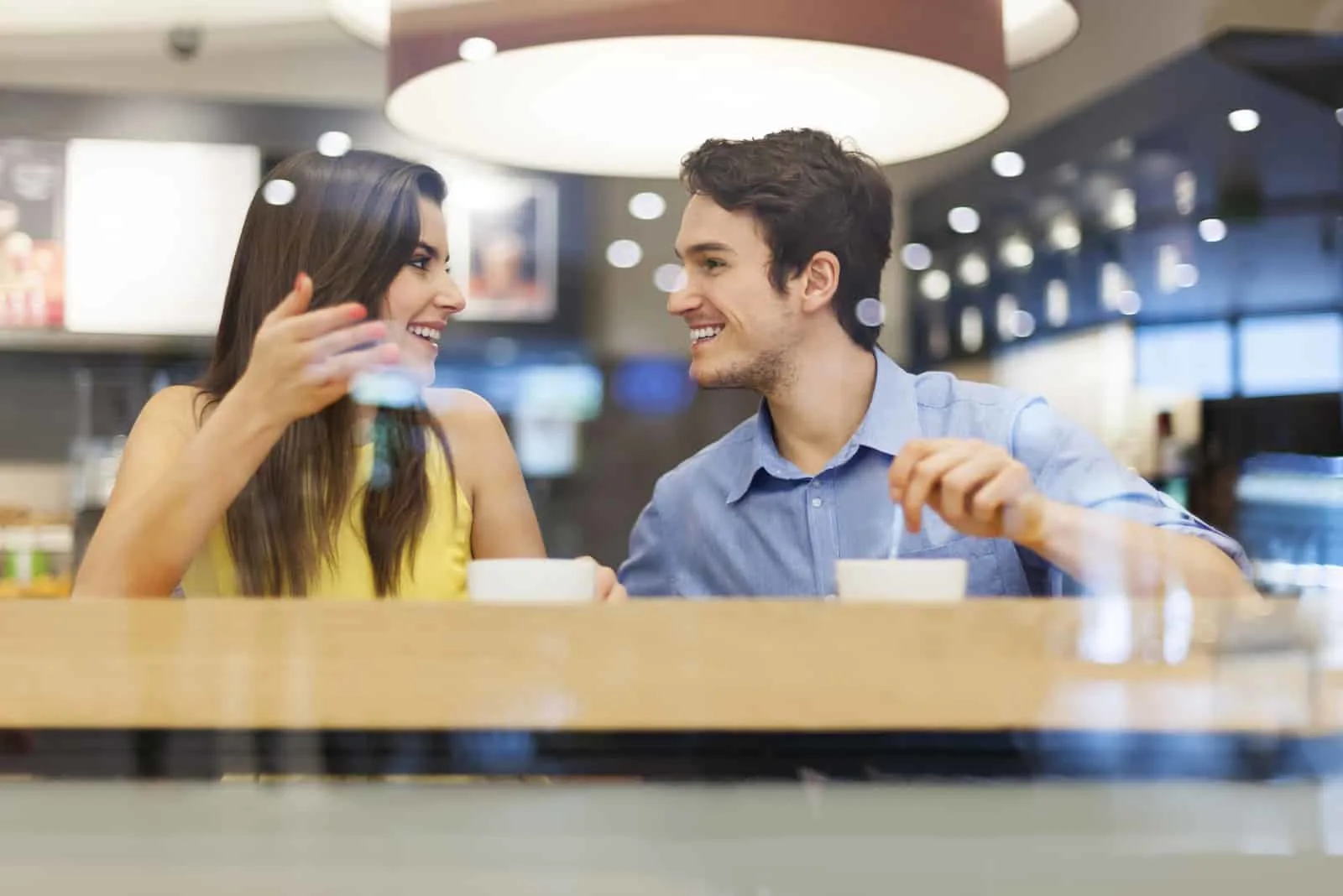 a smiling man and woman sit in a cafe and talk
