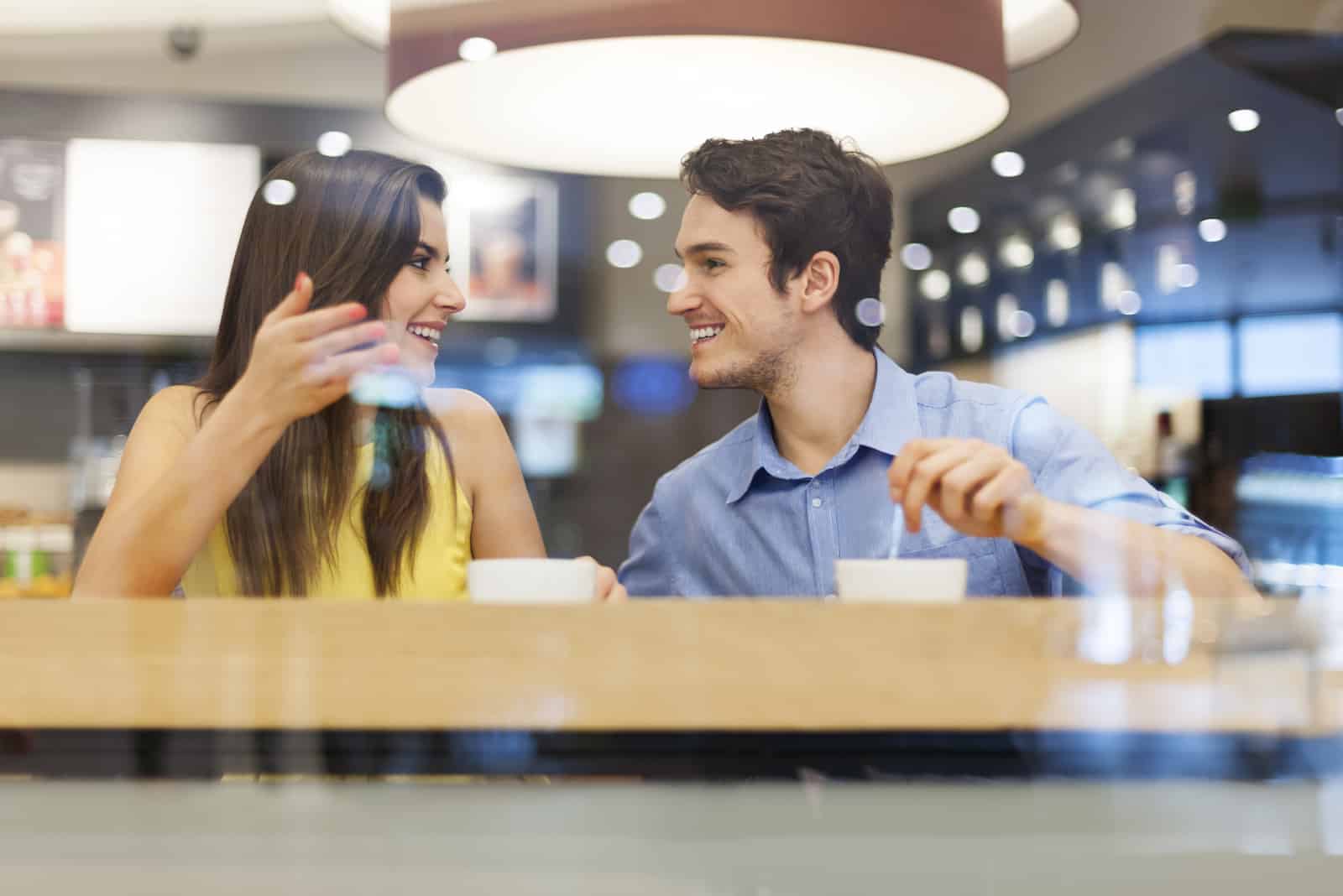 um homem e uma mulher sorridentes sentam-se num café e conversam