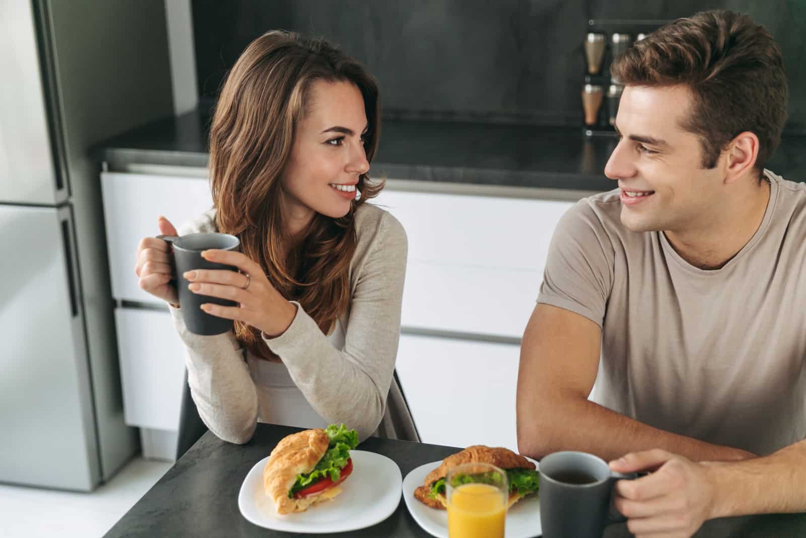 a smiling man and woman sitting in the kitchen talking