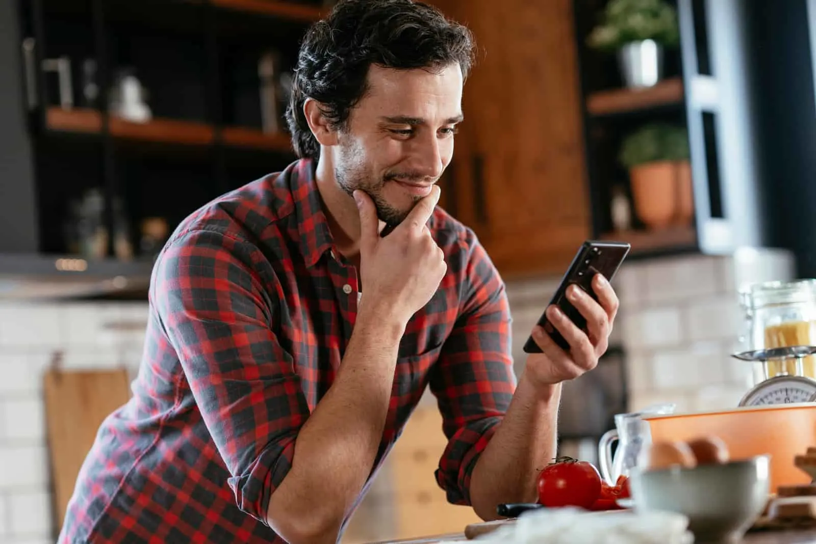 a smiling man leaning against the kitchen and holding a phone in his hand