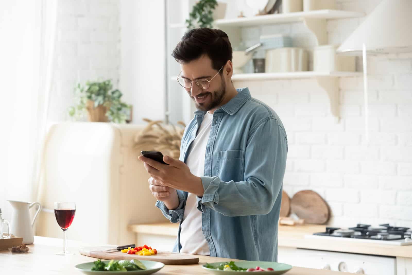 un uomo sorridente con gli occhiali in testa che sta in cucina e preme un pulsante del telefono