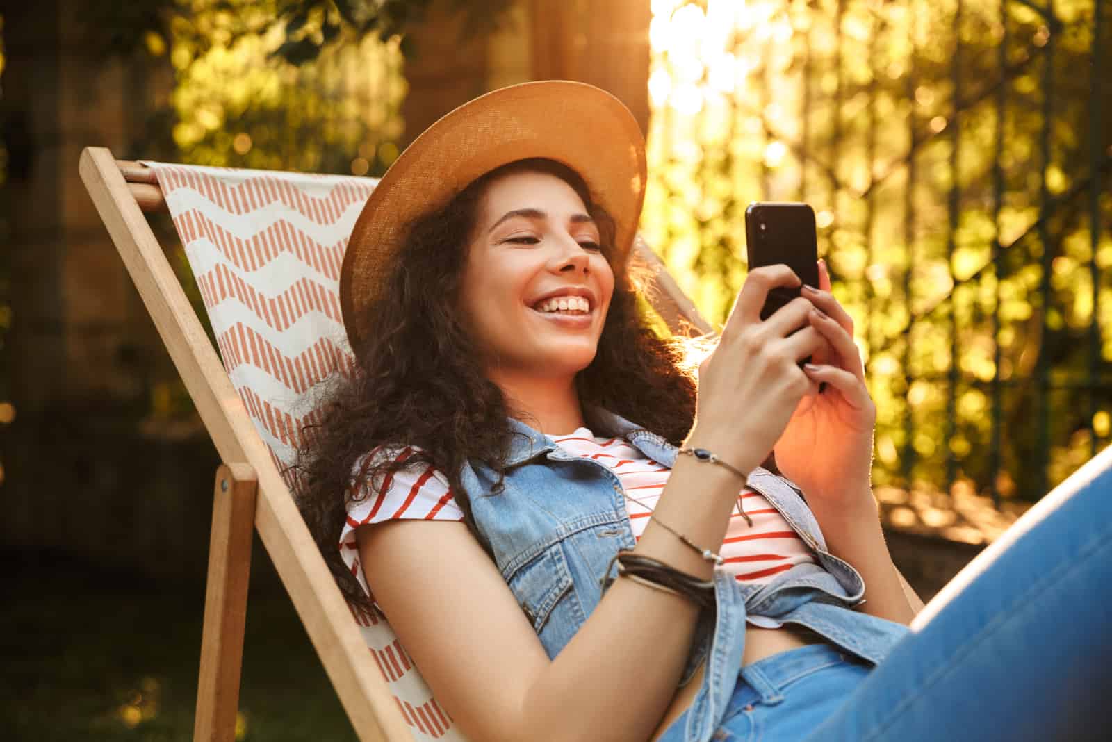 una mujer sonriente con un sombrero en la cabeza recostada en una silla y un botón en el teléfono