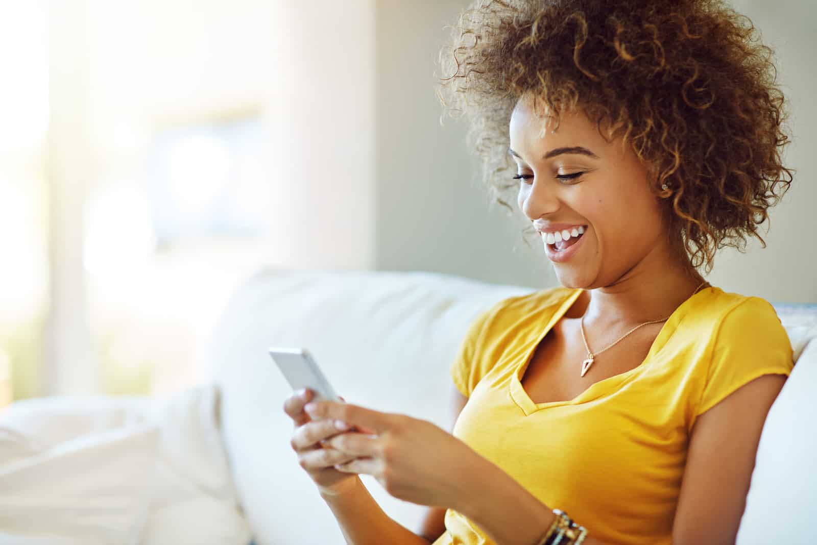 a smiling woman with frizzy hair sits and holds a mobile phone in her hand