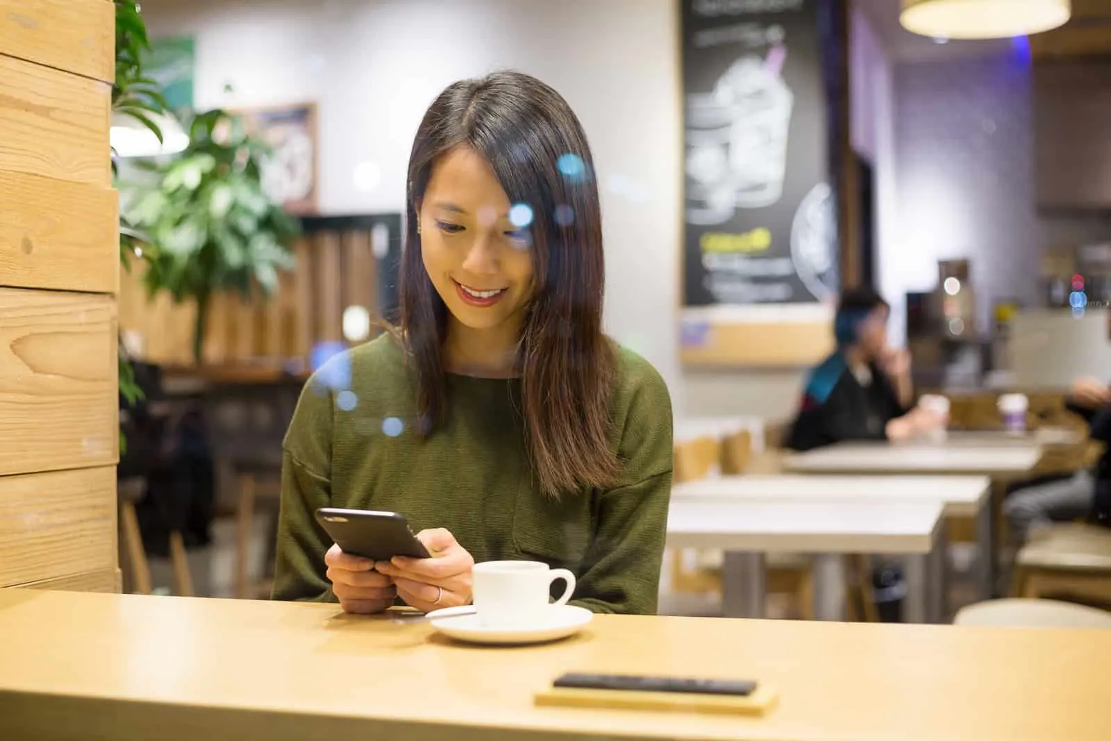 smiling girl sitting in a cafe and typing on the phone