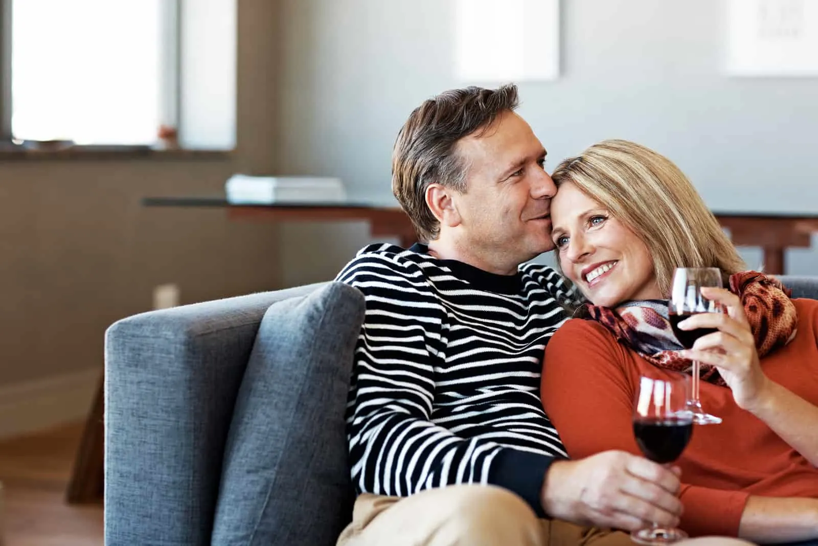 smiling mature couple sitting on their sofa drinking wine