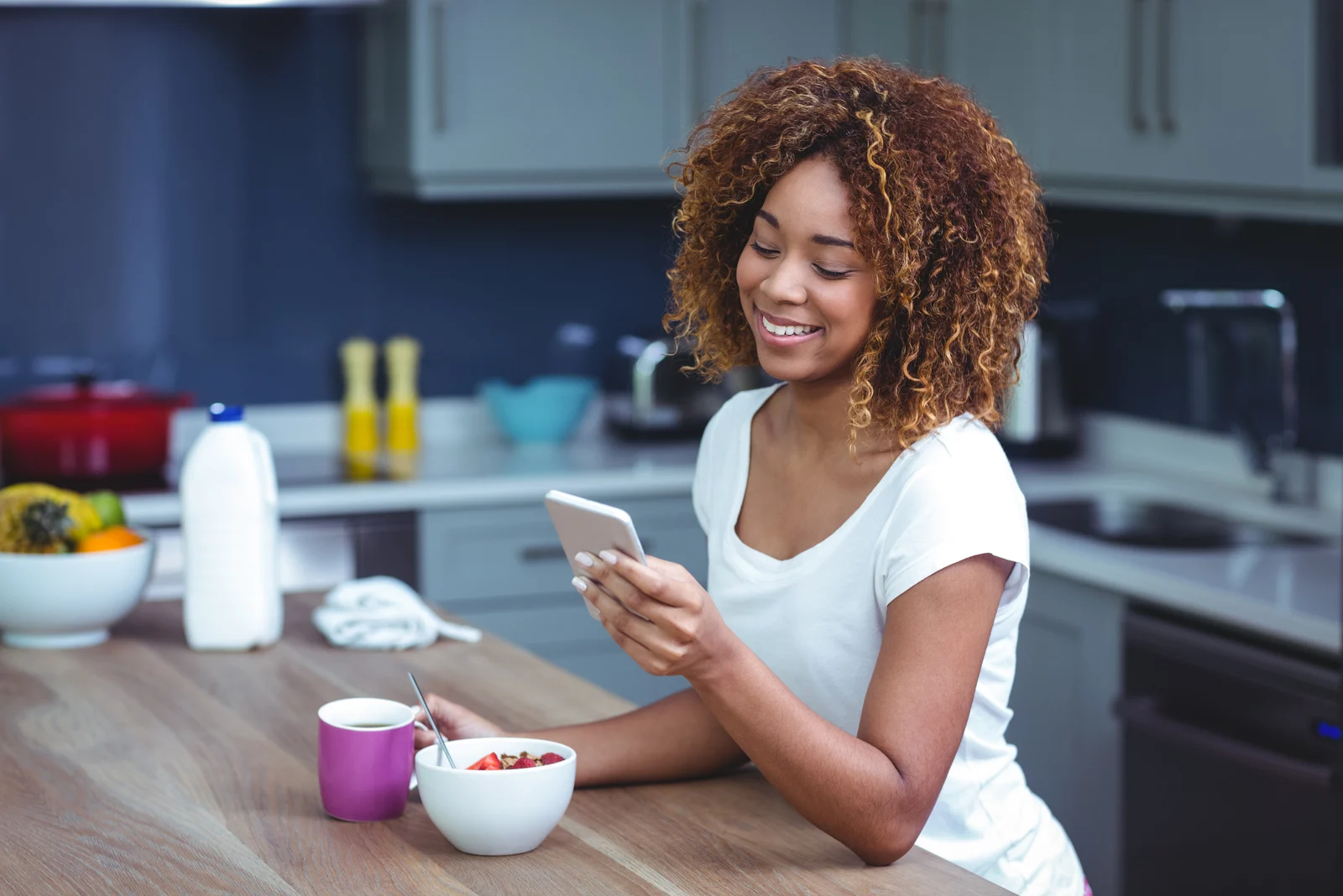 smiling woman sitting in the kitchen and pressing the phone