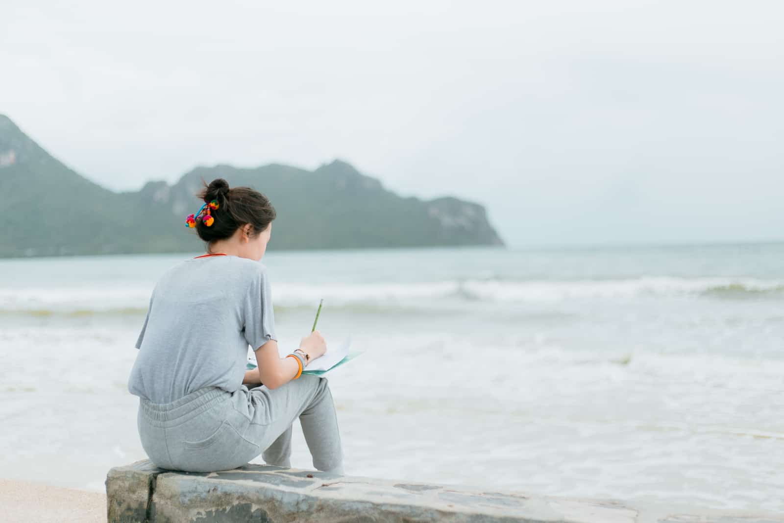woman sitting by beach and writing in notebook
