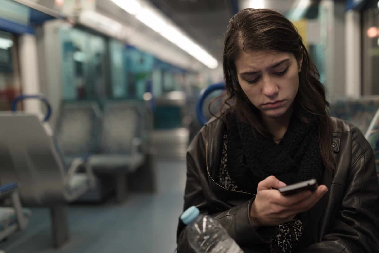 young woman sitting in train looking at her phone