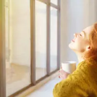 a beautiful woman sitting by the window drinking coffee
