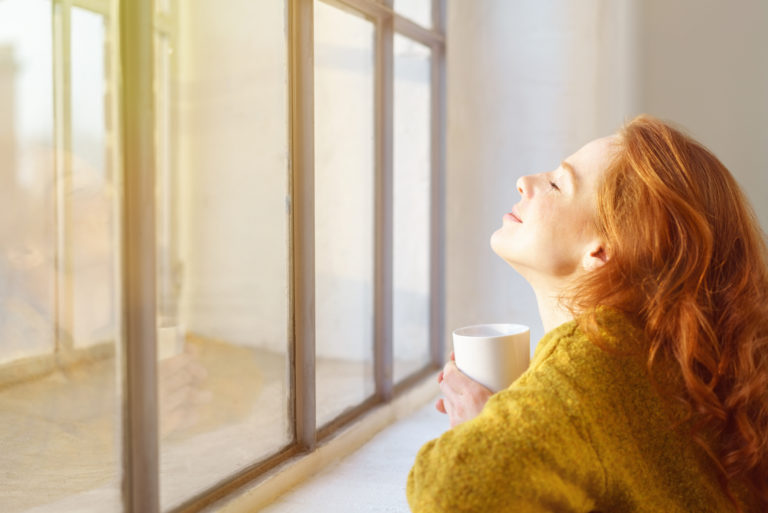 a beautiful woman sitting by the window drinking coffee