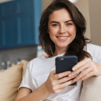 giovane donna sorridente con smartphone sul divano
